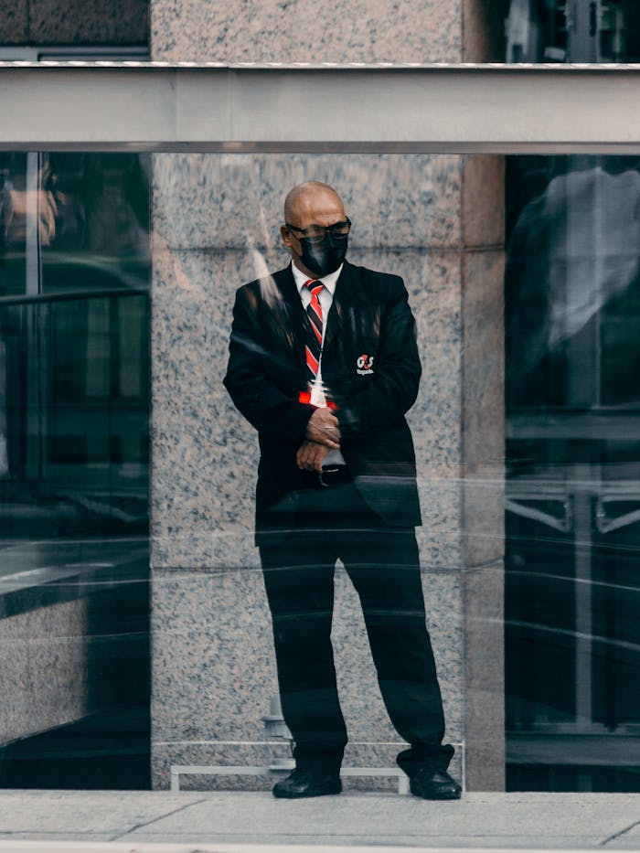 Bald security guard in black suit and tie stands in an urban environment, providing security.